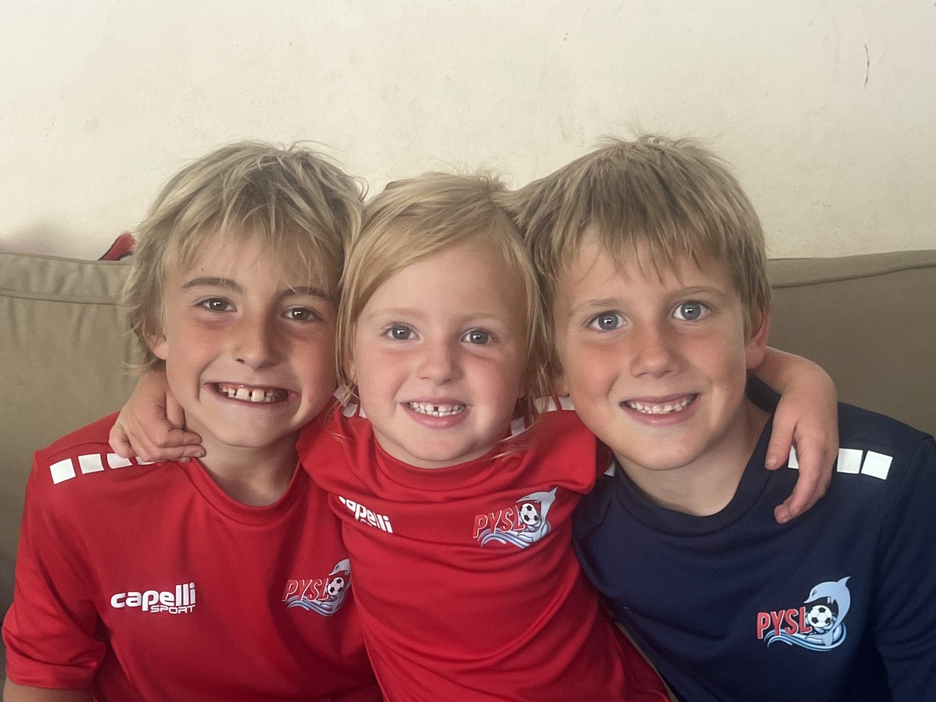 Three children smiling together in soccer jerseys